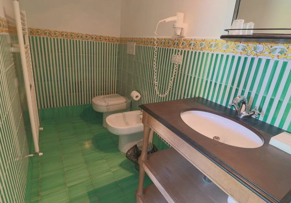 Bagno con piastrelle a righe verdi e gialle stile maiolica, asciugacapelli e mobile lavabo in legno scuro