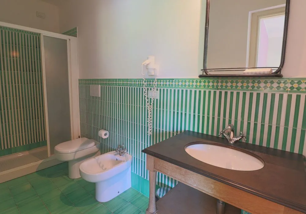 Bagno con piastrelle verdi a righe, doccia, bidet e mobile lavabo scuro con lavandino ovale