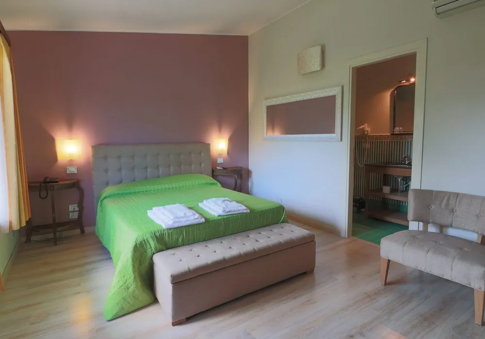 Camera con parete rosa, copriletto verde, testata capitonné e porta aperta sul bagno piastrellato di verde