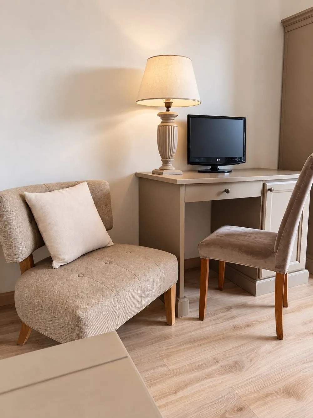 Angolo di una camera con poltroncina imbottita, scrittoio con lampada e piccolo televisore