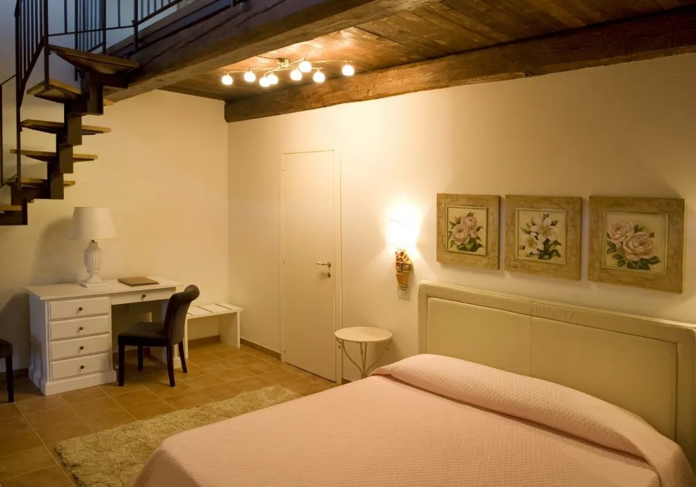 Loft bedroom with a pink bedspread, three floral prints and a wrought-iron spiral staircase