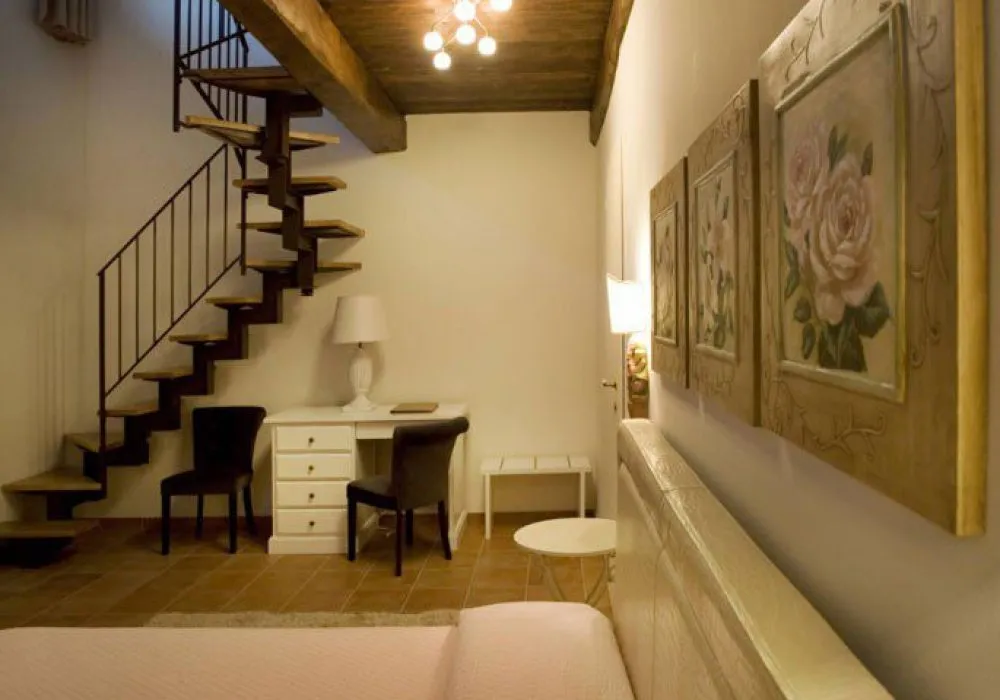 Scala in legno verso il soppalco, scrittoio bianco con lampada e tre grandi quadri di rose