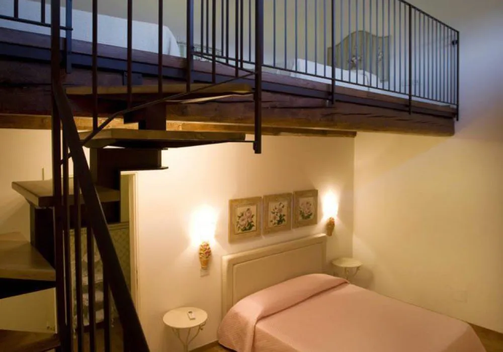 Soppalco con scala a chiocciola in ferro sopra il letto con copriletto rosa e quadretti floreali