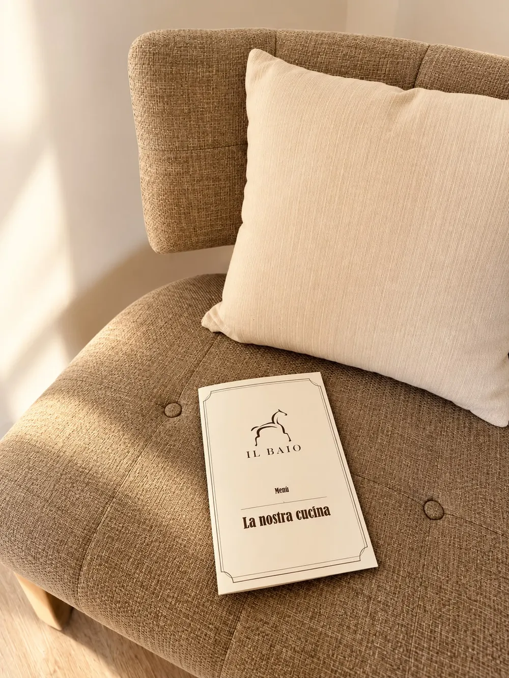 Il Baio restaurant menu resting on an armchair with a cushion, cream cover with the horse logo