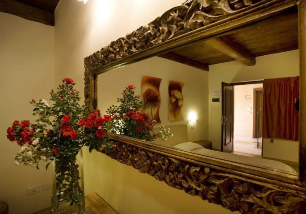 Specchio antico con cornice intagliata che riflette il soffitto a travi e una tenda rossa, vaso di rose rosse e bianche in primo piano