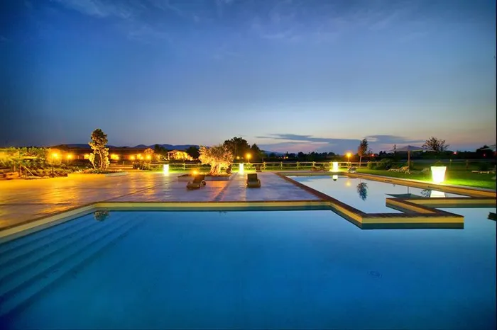 Piscina esterna illuminata al crepuscolo, con terrazza, lettini e lampade accese
