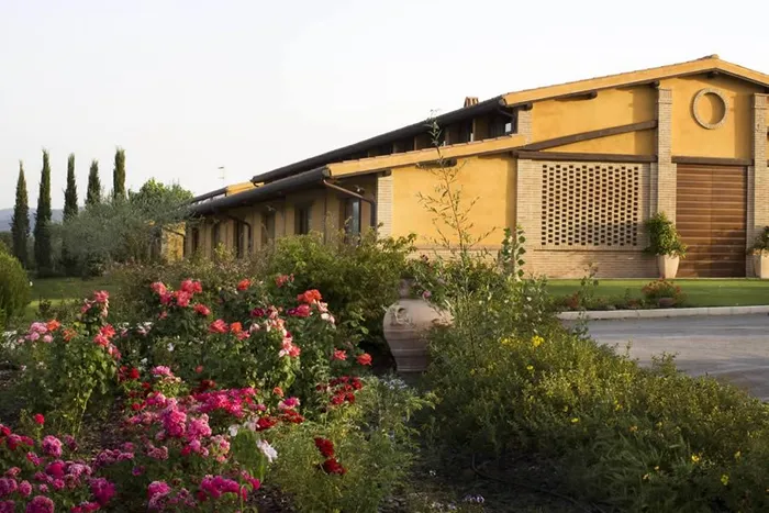 Aiuola di rose rosse e rosa in fiore davanti al casale giallo ocra