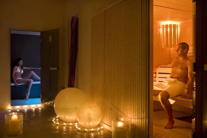 Zona sauna con candele e sfere luminose a terra, un uomo seduto nella cabina in legno