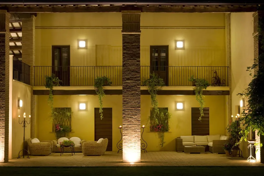 Loggia illuminata di sera con divani in vimini, candelabri accesi e piante ricadenti