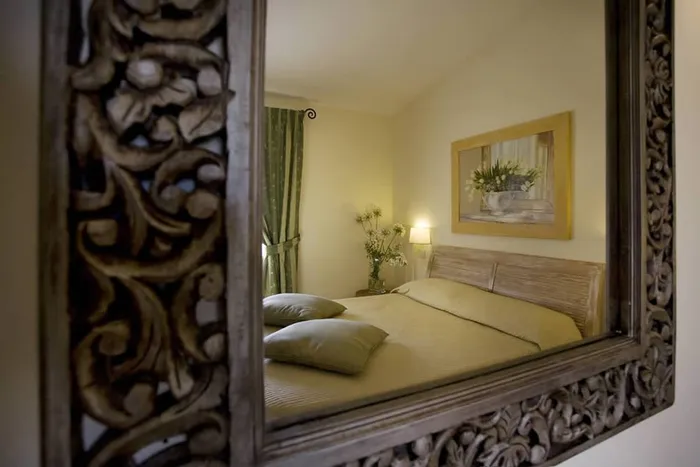 Specchio con cornice intagliata; nel riflesso il letto verde salvia e il quadro di tulipani
