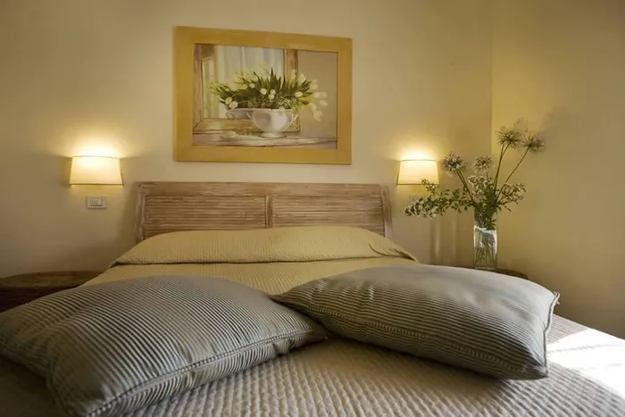 Testata in legno chiaro con cuscini a righe e quadro di tulipani bianchi sopra il letto