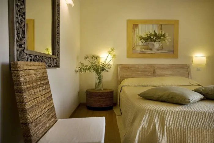 Angolo della camera con specchio intagliato, poltroncina in fibra e vaso di fiori bianchi
