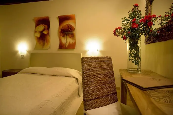 Camera con due tele di fiori sopra la testata, copriletto bianco e vaso di rose rosse