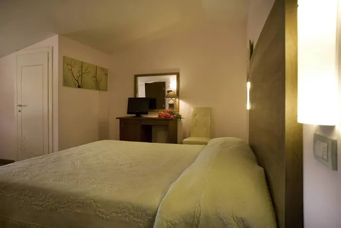 Letto con copriletto verde chiaro; sullo sfondo scrivania, specchio e quadro di rami fioriti