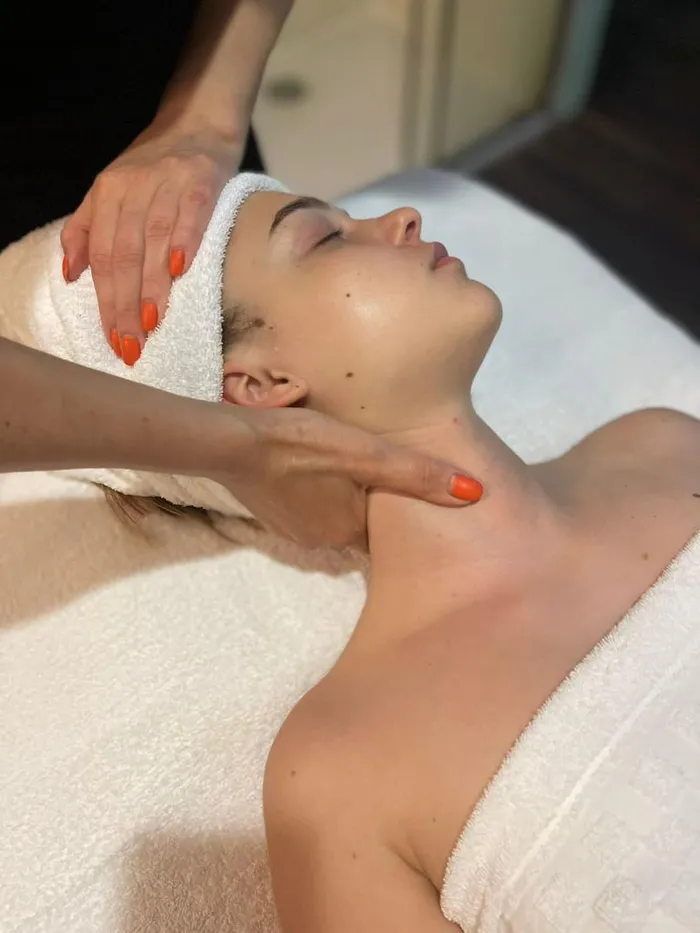 Massaggio al collo e al viso di una donna distesa, con fascia di spugna bianca
