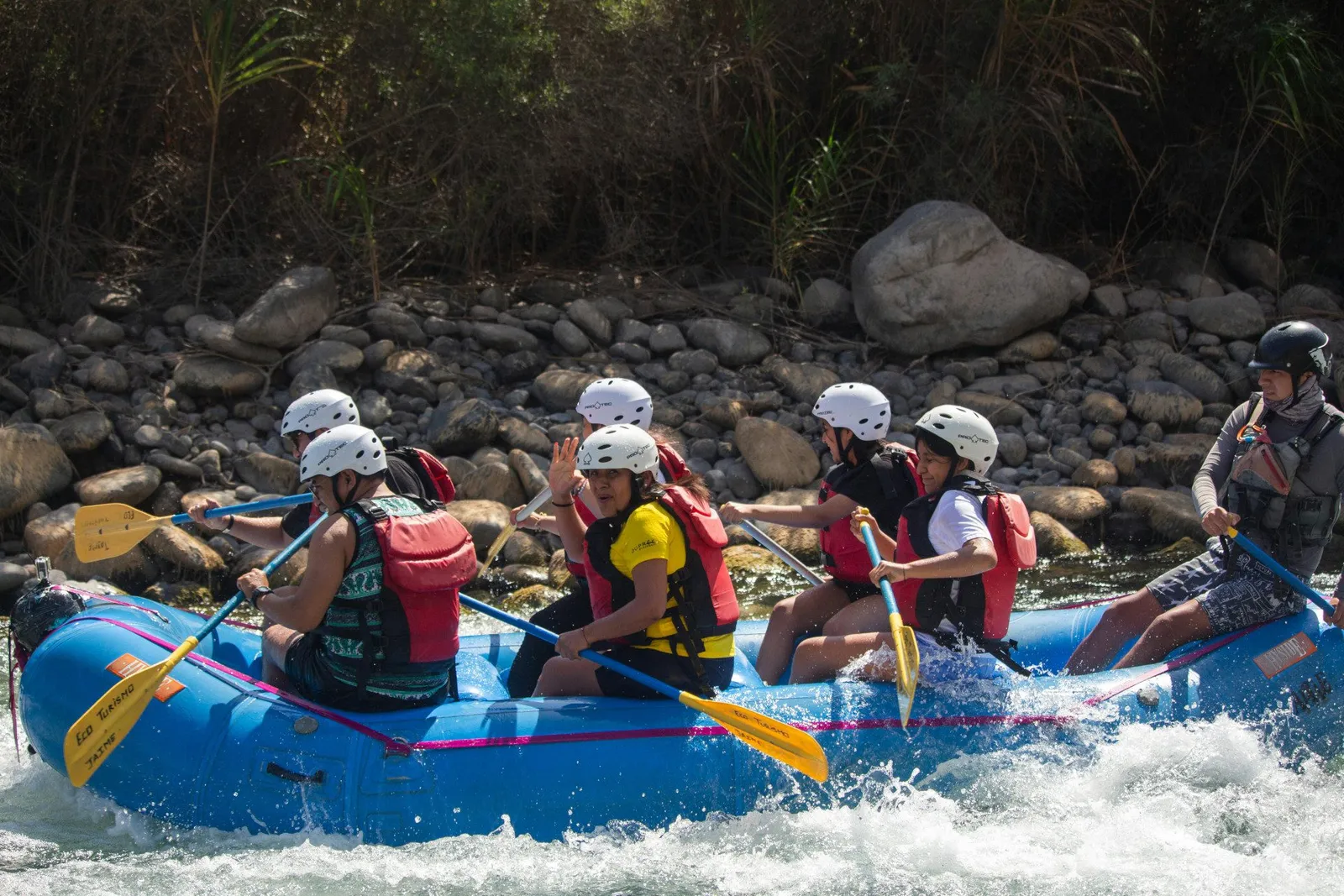 A crew in helmets and life jackets paddling a rafting boat through the rapids