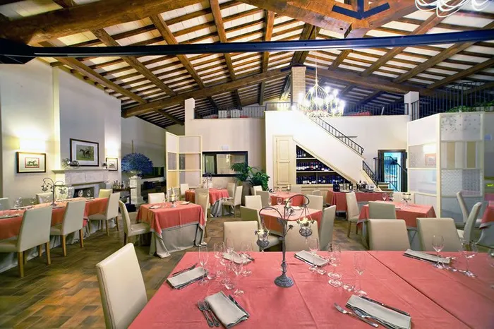 Sala del ristorante con capriate in legno, tovaglie color corallo e camino