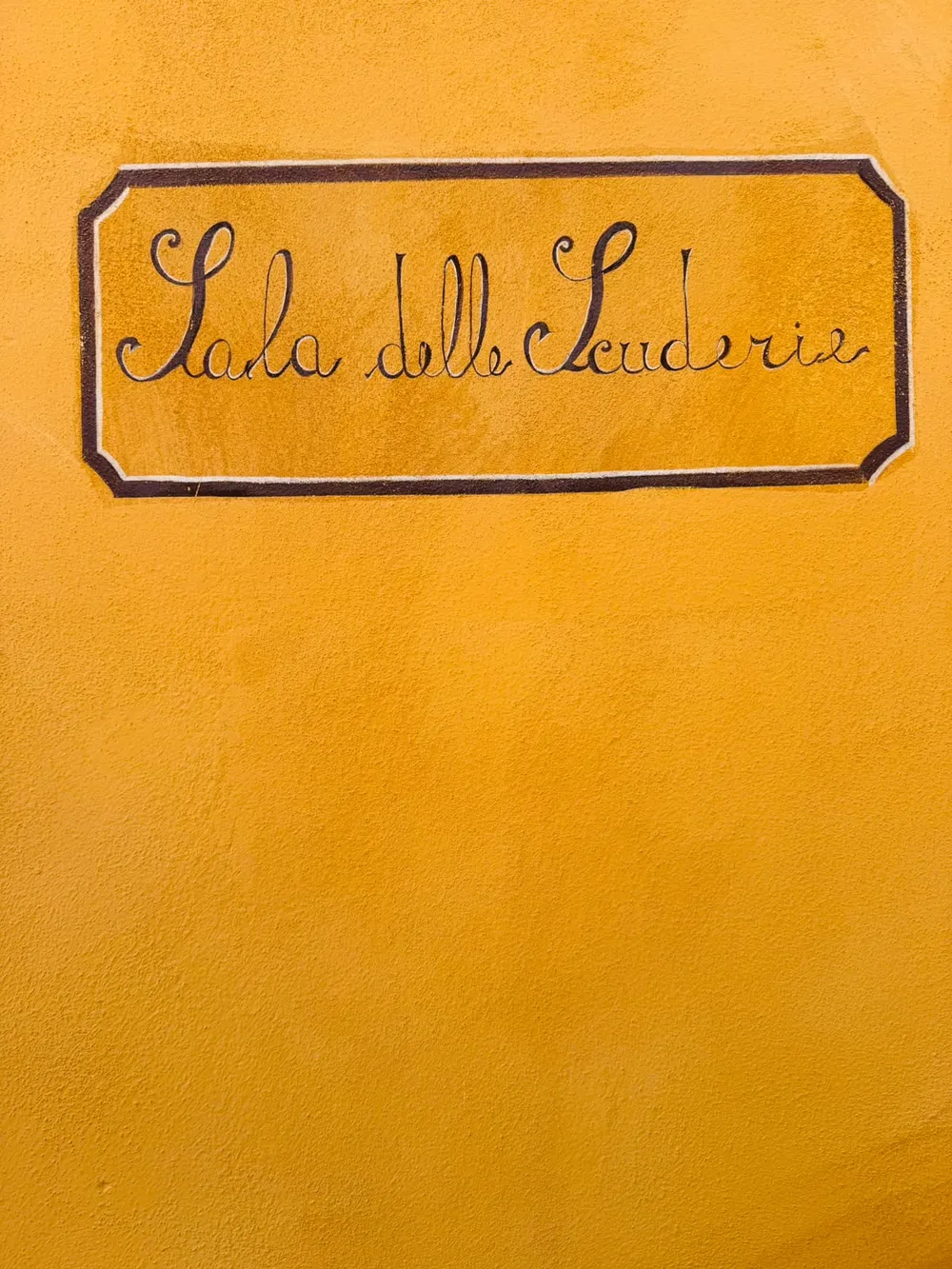 Hand-painted "Sala delle Scuderie" sign on a yellow wall
