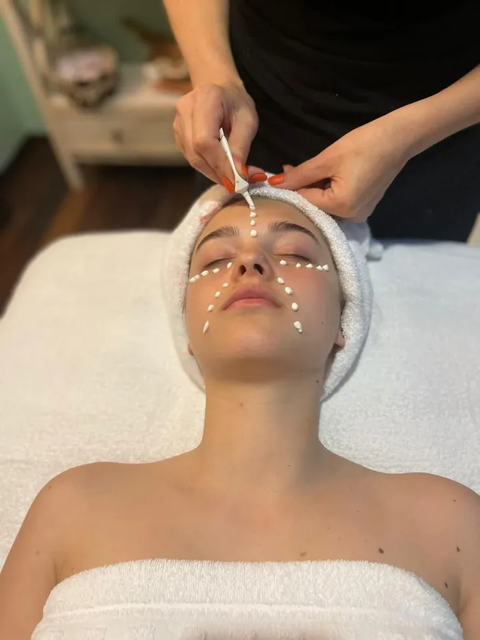 Estetista applica punti di crema sul viso di una cliente con fascia di spugna