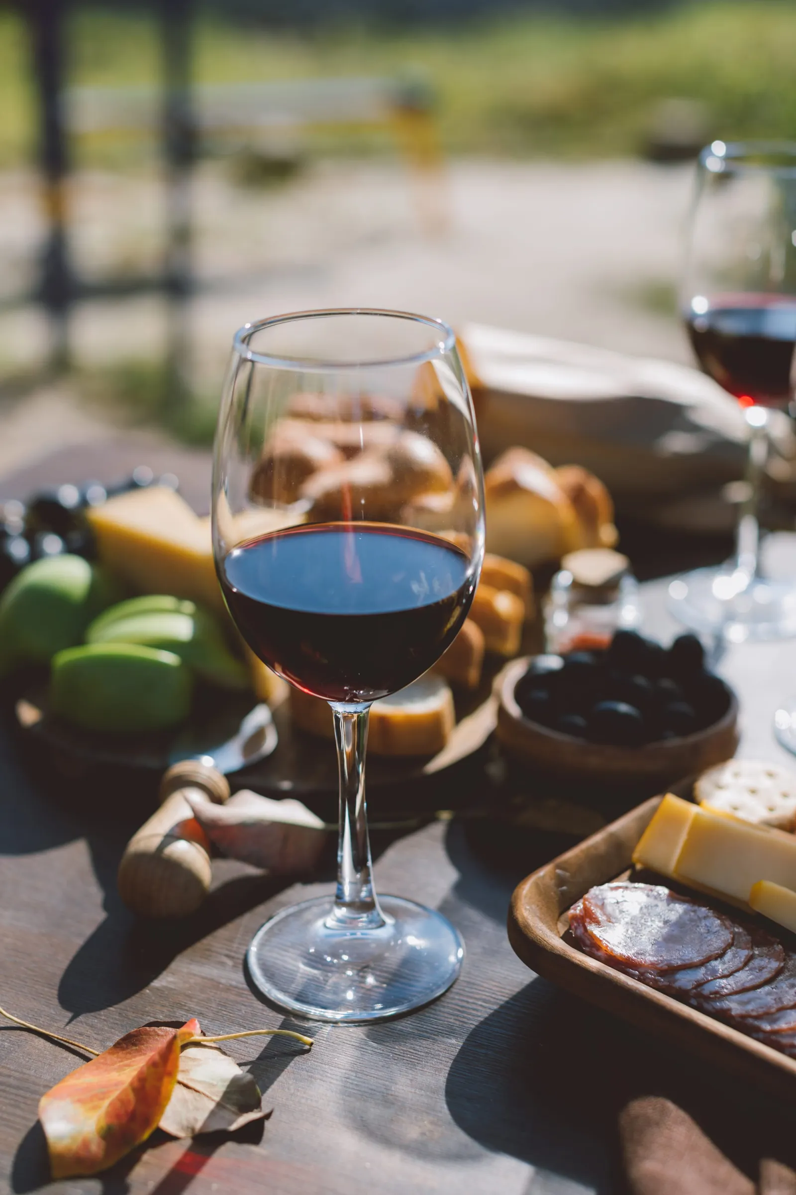 Glass of red wine on an outdoor table with cheese, cured meats and olives