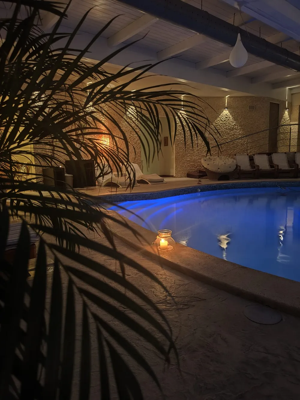 Indoor pool lit blue in the evening, with a lantern glowing on the rim